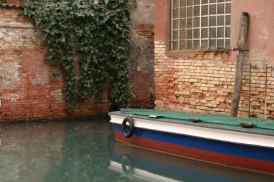 Boat on Venetian canal against wall of ivy.